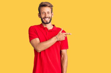 Yakışıklı sarışın, sakallı, günlük kıyafetler giyen, neşeli yüzlü, elleri ve parmaklarıyla yüzünü gösteren mutlu ve doğal bir ifade takınan bir adam. 