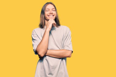 Uzun saçlı yakışıklı, günlük kıyafetler giyen, kameraya kendinden emin, kollarını kavuşturup gülümseyen ve çenesini kaldıran beyaz bir adam. Olumlu düşünmek. 