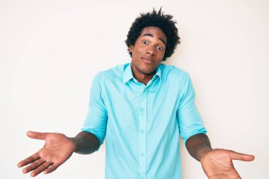 Yakışıklı Afro saçlı, sıradan kıyafetler giyen, elleri ve kolları havada kafası karışmış afro-amerikalı bir adam. şüphe kavramı. 
