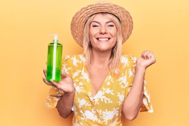 Yazlık şapkalı, elinde aloe vera kremiyle gezen güzel sarışın kadın gururla bağırıyor, zaferi kutluyor ve başarıyı kollarını kaldırarak kutluyor.