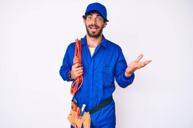 Kıvırcık saçlı, ayı kılıklı, işçi tulumu giyen ve elektrik kabloları takan yakışıklı genç adam başarıyı mutlu bir gülümsemeyle ve kazanan ifadeyle el kaldırarak kutluyor. 