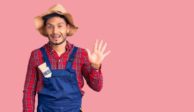 Yakışıklı Latin Amerikalı genç adam, becerikli adam üniforması giyiyor ve beş numarayı gösterip işaret ederken kendine güvenen ve mutlu.. 