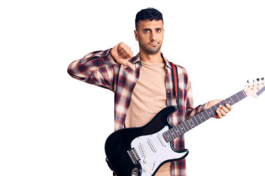Öfkeli yüzüyle elektro gitar çalan genç İspanyol adam, olumsuz işaret baş parmakları aşağıda, reddedilme konsepti 