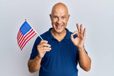 Orta yaşlı kel adam, elinde Birleşik Devletler bayrağı var. Parmaklarıyla imza atıyor, gülümsüyor. Mükemmel bir sembol. 