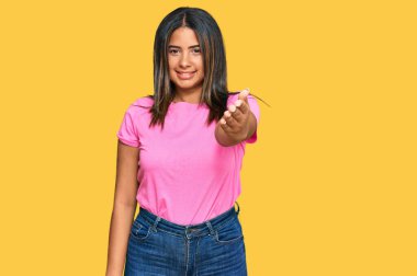 Gündelik kıyafetler giyen genç Latin kız dostça bir selamlama ve hoş geldin hediyesi olarak el sıkışmayı sunuyor. başarılı iş. 