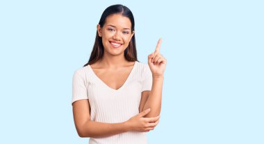 Gündelik beyaz tişört giyen genç, güzel Latin kız gülümsüyor mutlu bir şekilde elini ve parmağını yana uzatıyordu. 