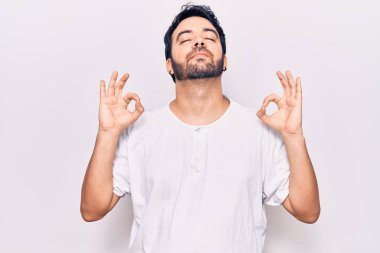 Günlük kıyafetler giyen genç İspanyol adam rahatla ve gözleri kapalı gülümse parmaklarıyla meditasyon hareketi yapıyor. yoga konsepti. 