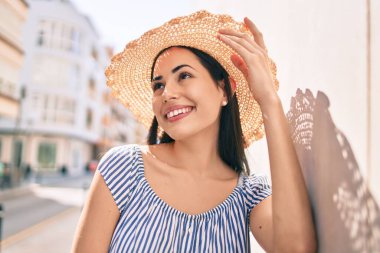 Tatildeki genç Latin turist kız gülümsüyor. Şehrin duvarına yaslanmaktan mutlu..
