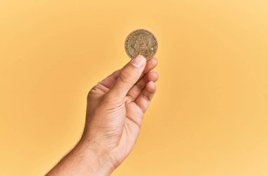 Genç İspanyol el, bitcoin 'i izole edilmiş sarı arka planda tutuyor..