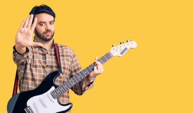 Genç İspanyol adam elektro gitar çalıyor. Açık elle. Dur işareti yapıyor. 