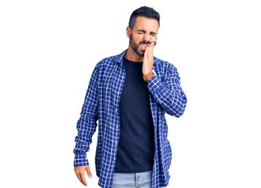 Günlük kıyafetler giyen genç İspanyol adam diş ağrısı ya da diş hastalığından dolayı acı dolu bir ifadeyle ağıza dokunuyor. dişçi 