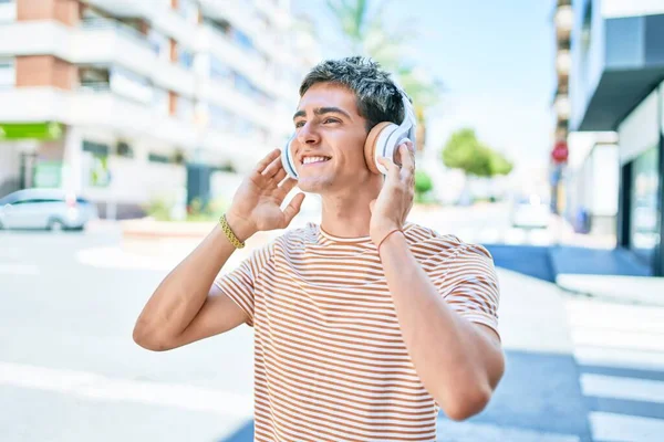 若いですハンサムなCaucasian男笑顔幸せな音楽を聞いて使用してヘッドフォンで街を歩く — ストック写真