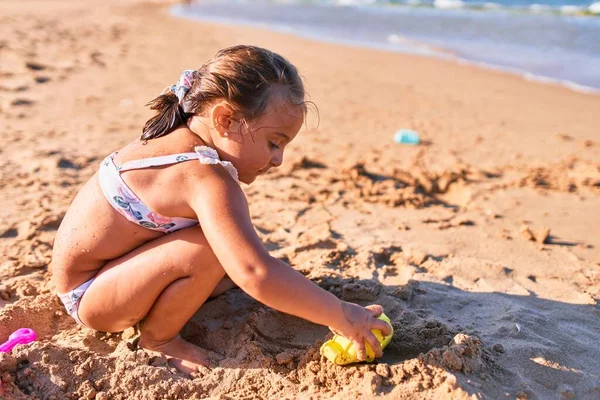 ビキニを着た愛らしいブロンドの子供 ビーチでバケツやシャベルを使用して砂の城を構築する — ストック写真