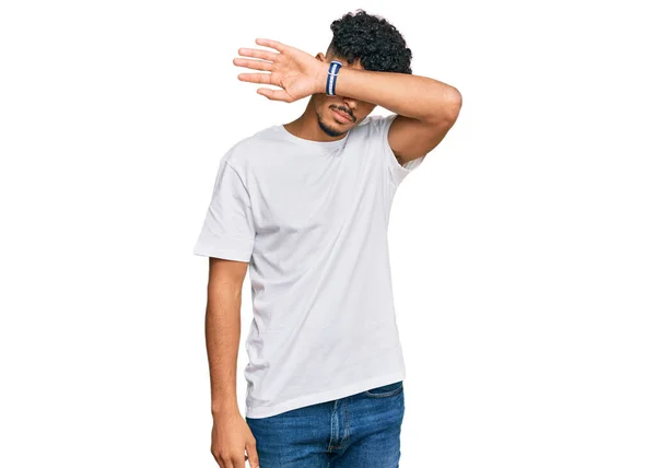 年轻的阿拉伯男子穿着宽松的白色T恤 用胳膊蒙住眼睛 看起来严肃而忧郁 躲藏和拒绝的概念 — 图库照片