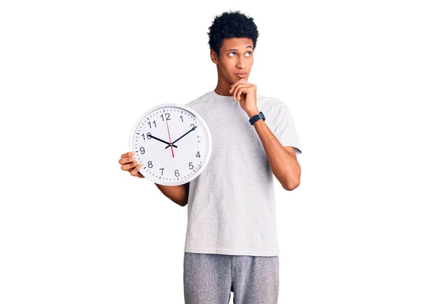 Młody Afroamerykanin Trzymający Wielki Zegar Poważna Twarz Myślący Pytaniu Ręką — Zdjęcie stockowe
