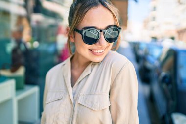 Genç, güzel, sarışın, beyaz bir kadın güneşli bir günde mutlu bir şekilde gülümsüyor.