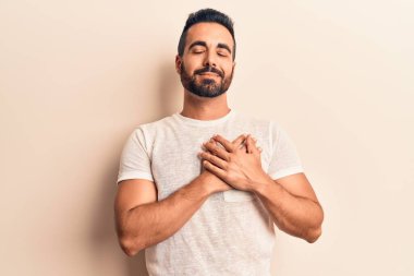 Gündelik kıyafetler giyen genç İspanyol adam elleri göğsünde gülümsüyor, gözleri kapalı ve yüzünde minnet ifadesi var. sağlık kavramı. 