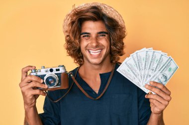 Klasik kamera ve dolar tutan genç İspanyol adam yüzünde mutlu ve havalı bir gülümsemeyle gülümsüyor. diş gösterme. 