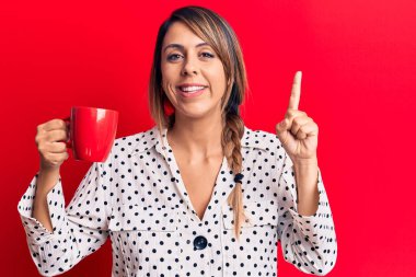 Genç ve güzel bir kadın bir fikir veya soruyla gülümseyen bir kupa kahve içiyor. 