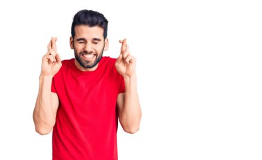 Sakallı, sıradan bir tişört giyen, umut dolu ve gözleri kapalı bir şekilde gülümseyerek el hareketi yapan genç yakışıklı bir adam. Şans ve batıl inançlar. 