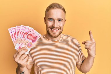 Kafkasyalı genç bir adam elinde 100 yuan Çin banknotları ile bir fikir veya soru işareti ile gülümsüyor. 