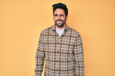 Yakışıklı, sakallı, sıradan kıyafetler giyen, kameraya seksi bir ifadeyle bakan, neşeli ve mutlu yüzlü bir adam.. 