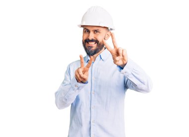 Mimar şapkası takan yakışıklı genç adam kameraya bakıp zafer işareti yapıyor. İki numara.. 