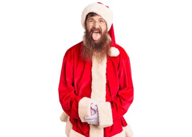 Uzun sakallı, Noel Baba kostümü giyen yakışıklı, genç, kızıl saçlı, komik bir ifadeyle dilini dışarı çıkaran adam. duygu kavramı. 