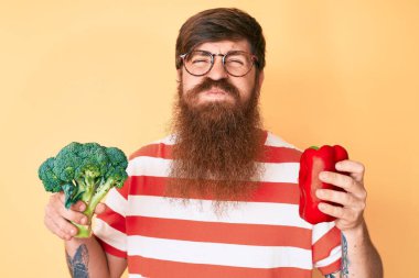 Uzun sakallı, elinde brokoli ve komik suratlı kırmızı biber şişiren yanaklı yakışıklı genç bir adam. Ağzı havayla şişer, havayı yakalar.. 