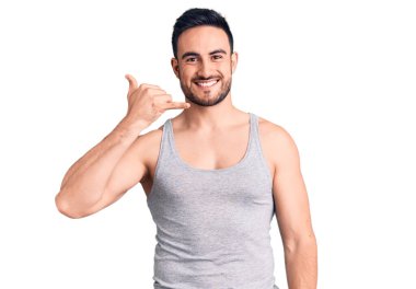 Mayo ve kolsuz tişört giyen genç yakışıklı adam telefonla el ve parmak hareketleriyle gülümsüyor telefonda konuşur gibi. iletişim kavramları. 