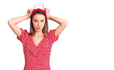 Elbise ve diadem giyen genç güzel bir kız parmaklarıyla boynuz gibi komik hareketler yapıyor. 