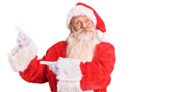 Gri saçlı, uzun sakallı, geleneksel Noel Baba kostümü giyen, gülümseyen ve kameraya bakan yaşlı bir adam.. 