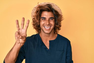 Yaz şapkası takan İspanyol genç adam üç numarayı gösterip işaret ederken kendinden emin ve mutlu bir şekilde gülümsüyor.. 