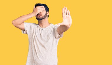Latin kökenli genç bir adam, günlük kıyafetler giyip, elleriyle gözlerini kapatıyor ve üzgün ve korku ifadeleriyle jestleri durduruyor. utangaç ve olumsuz kavram. 
