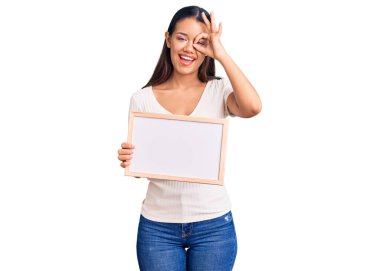 Genç, güzel, Latin bir kız elinde boş beyaz bir karatahta tutarken gülümsüyor. 