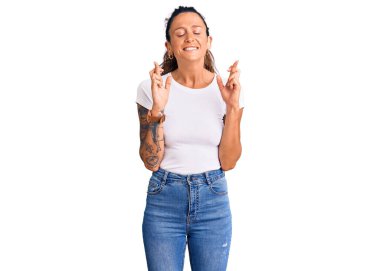 Dövmeli, beyaz tişörtlü, umut dolu ve gözleri kapalı bir şekilde gülümseyen genç İspanyol kadın. Şans ve batıl inançlar. 