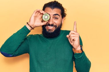 Elinde kivi tutan genç Arap adam bir fikir veya soruyla gülümsüyor ve mutlu bir yüzle işaret ediyor. 