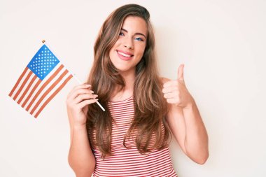 Amerika Birleşik Devletleri bayrağı taşıyan güzel beyaz kadın mutlu ve olumlu gülümsüyor, başparmağıyla mükemmel ve onay işareti yapıyor. 