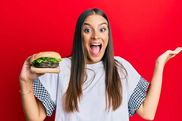 Fiatal Spanyol Eszik Hamburger Ünnepli Győzelem Boldog Mosollyal Győztes Kifejezés — Stock Fotó