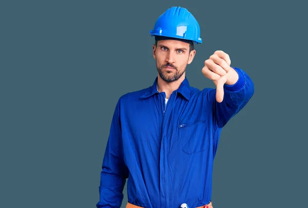 Young handsome man wearing worker uniform and hardhat afraid and terrified with fear expression stop gesture with hands, shouting in shock. panic concept.