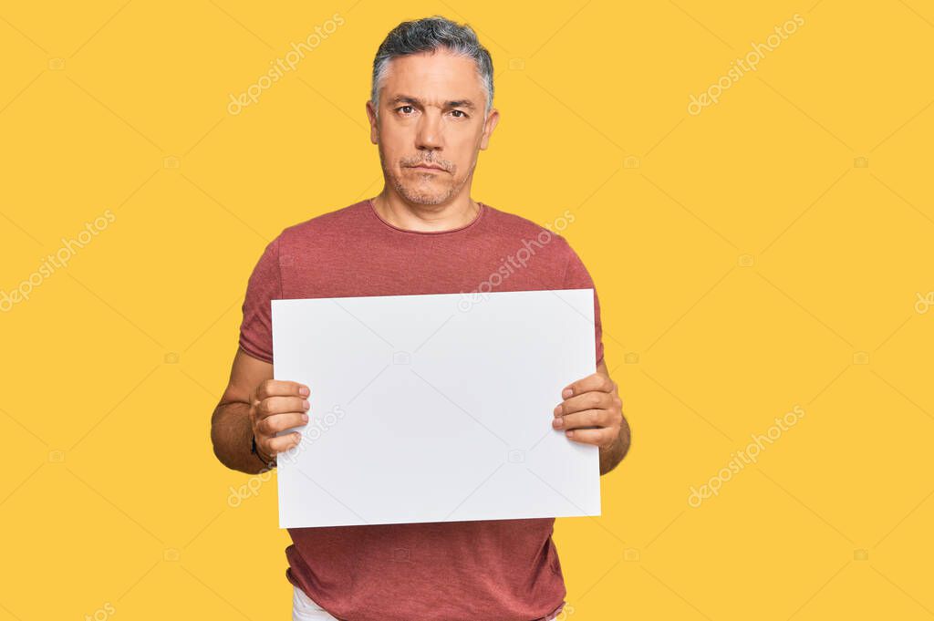 Handsome middle age man holding blank empty banner thinking attitude and sober expression looking self confident 