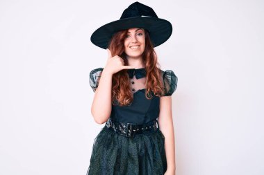 Cadı cadılar bayramı kostümü giymiş genç ve güzel bir kadın gülümsüyor telefonla el ve parmaklarıyla jest yapıyor telefonda konuşuyor gibi. iletişim kavramları. 