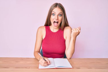 Masaya oturup gururla bağıran, zafer ve başarıyı kutlayan beyaz bir kız. Kollarını kaldırarak heyecanla bekliyor. 