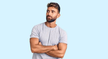 Sıradan kıyafetler giyen genç İspanyol adam kollarını kavuşturmuş ve kendinden emin bir şekilde yan tarafa bakıyor. 