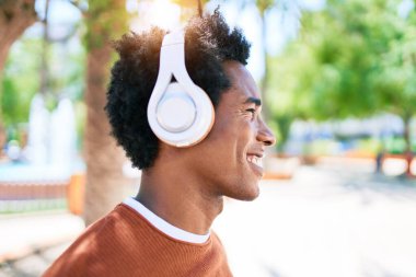 Genç yakışıklı Afro-Amerikan adam kulaklıkla müzik dinliyor. Yüzünde gülümsemeyle kasaba caddesinde yürürken.