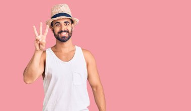 Yaz şapkası takan İspanyol genç adam üç numarayı gösterip işaret ederken kendinden emin ve mutlu gülümsüyor.. 