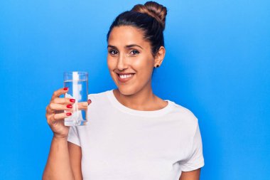 Genç, güzel esmer kadın bir bardak su içiyor. Pozitif ve mutlu görünüyor. Kendine güvenen bir gülümsemeyle dişlerini gösteriyor. 