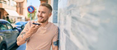 Genç İrlandalı gülümseyen mutlu bir adam şehrin caddesinde akıllı telefonda konuşuyor..