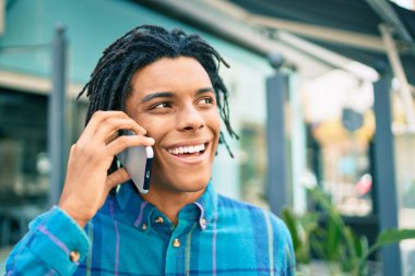 Genç Afrikalı Amerikalı gülümseyen mutlu bir adam şehrin caddesinde akıllı telefondan konuşuyor..