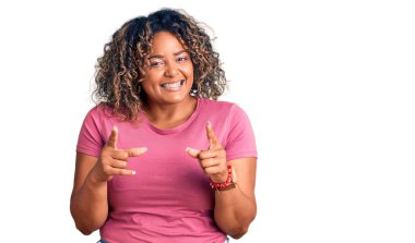 Genç Afro-Amerikan artı cüsseli kadın gündelik kıyafetler giyip mutlu ve komik yüzlü parmakları kameraya doğrultuyor. iyi enerji ve titreşimler. 